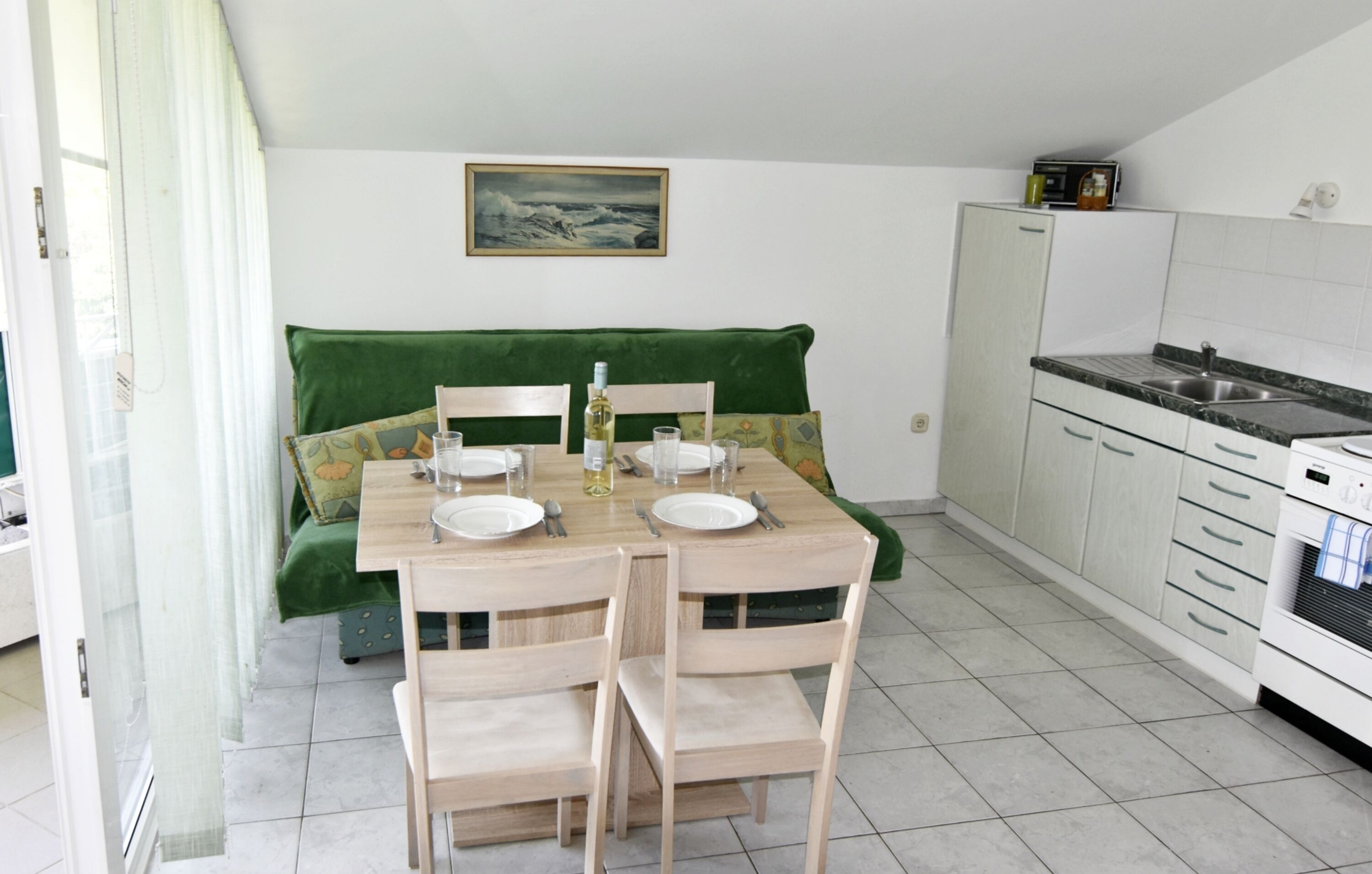 A compact kitchen with a dining table set for two, a green sofa, and a painting on the wall.