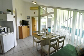 A dining area with a table set for four, a television, and a kitchen area with a refrigerator and microwave. - Prime Location Apartment Nicely Equipped (Umag)