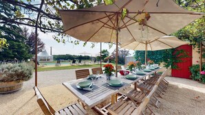 Un espace de restauration en plein air avec une table dressée pour quatre personnes, entourée de chaises en bois, sous un grand parasol.