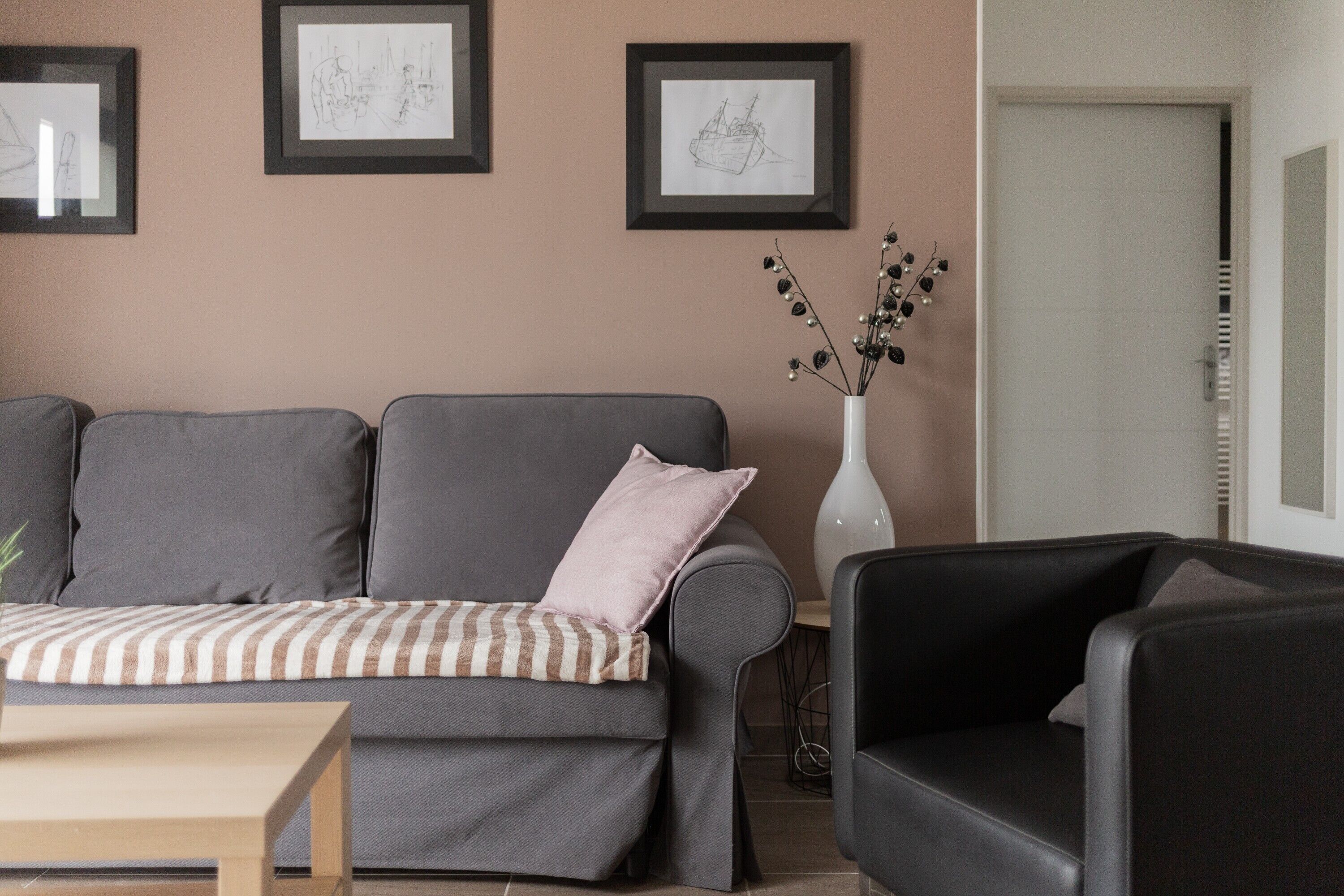 Un soggiorno con un divano grigio, una coperta a righe, un vaso bianco con rami e opere d'arte incorniciate al muro.