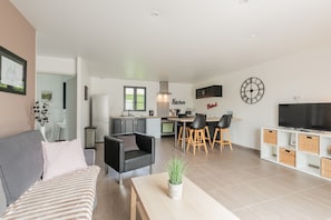 Una sala de estar moderna con un sofá, un comedor con sillas, una cocina con armarios y un televisor sobre un mueble.