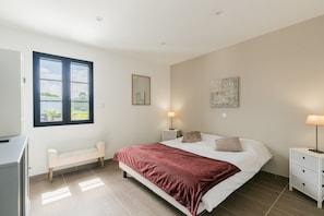 Ein Schlafzimmer mit einem Bett, Nachttischen, einer Bank, einem Fenster und einem an der Wand befestigten Kunstwerk.