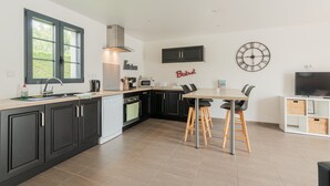 Une cuisine moderne avec des meubles de rangement noirs, une table à manger en bois et une horloge au mur.