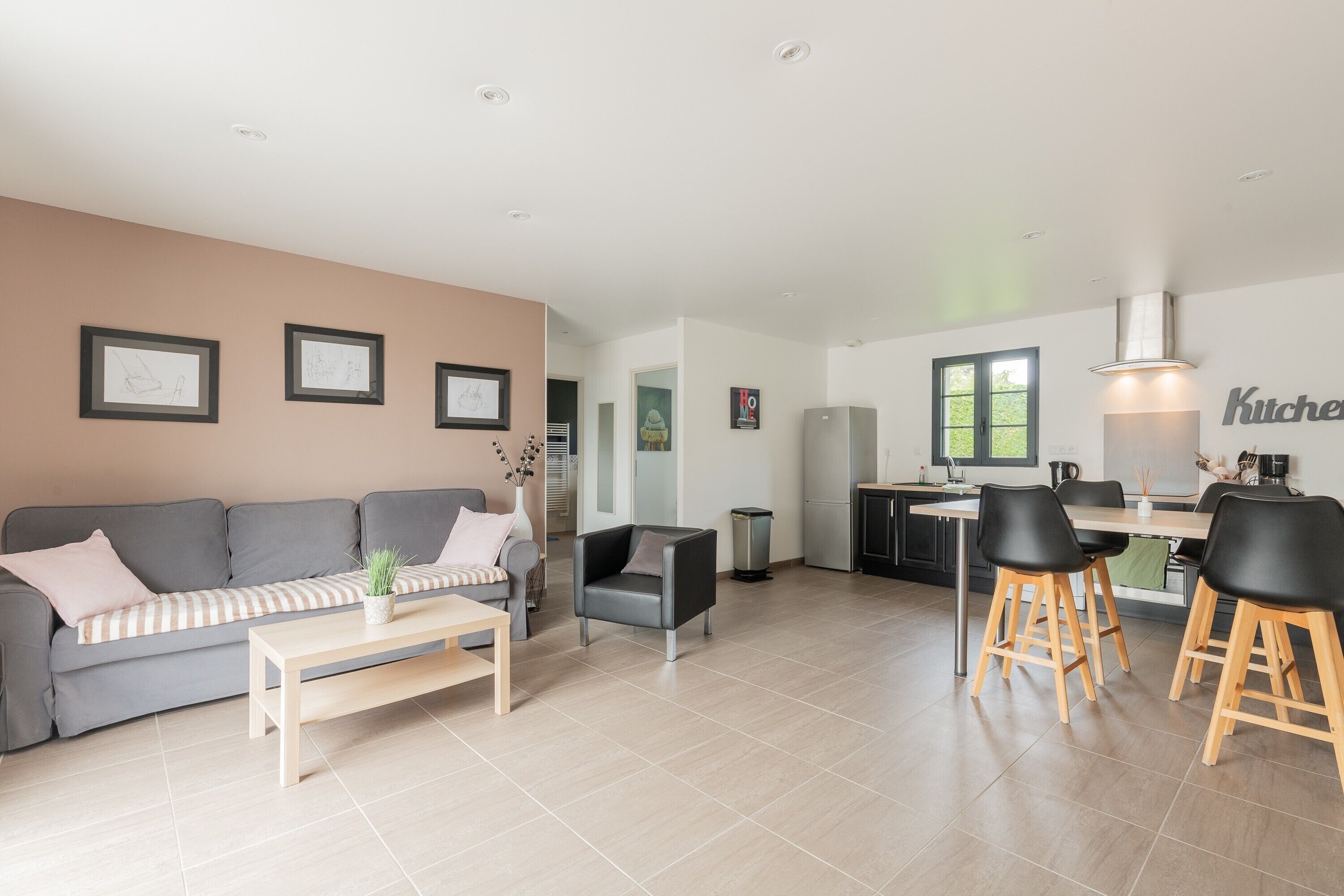 Un salon moderne avec un canapé, une table basse et un coin repas comprenant des chaises, et une cuisine en arrière-plan.