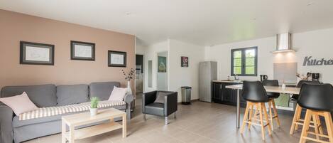 A modern living room with a sofa, coffee table, and a dining area with chairs and a kitchen in the background.