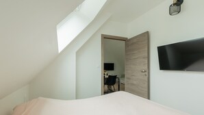 A bedroom with a bed, a TV mounted on the wall, a door leading to another room, and a skylight. - Vacation Rental Le Filou (Saint-Quentin-en-Tourmont)