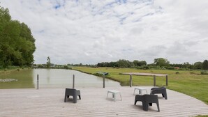A wooden deck with outdoor seating and a view of a calm body of water. - Vacation Rental Le Filou (Saint-Quentin-en-Tourmont)