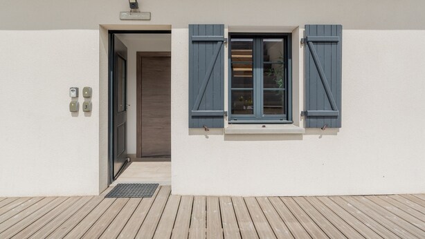Ein Gebäudeeingang mit Tür, Fenster mit Rollläden und Briefkasten.
