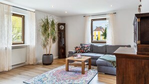Ein Wohnzimmer mit Sofa, Couchtisch, Topfpflanze, einer Uhr und Blick ins Freie.