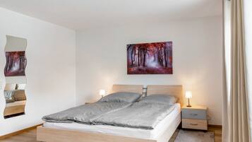 Une chambre à coucher moderne avec un lit en bois, une table de chevet avec une lampe, un tableau accroché au mur et un miroir.