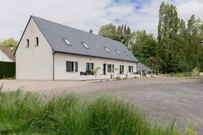 A single-story building with a sloped roof, multiple windows, and a paved driveway. - Holiday Home 'Le T'chot Pierre 2' with Lake View, Private Terrace and Wi-Fi (Saint-Quentin-en-Tourmont)