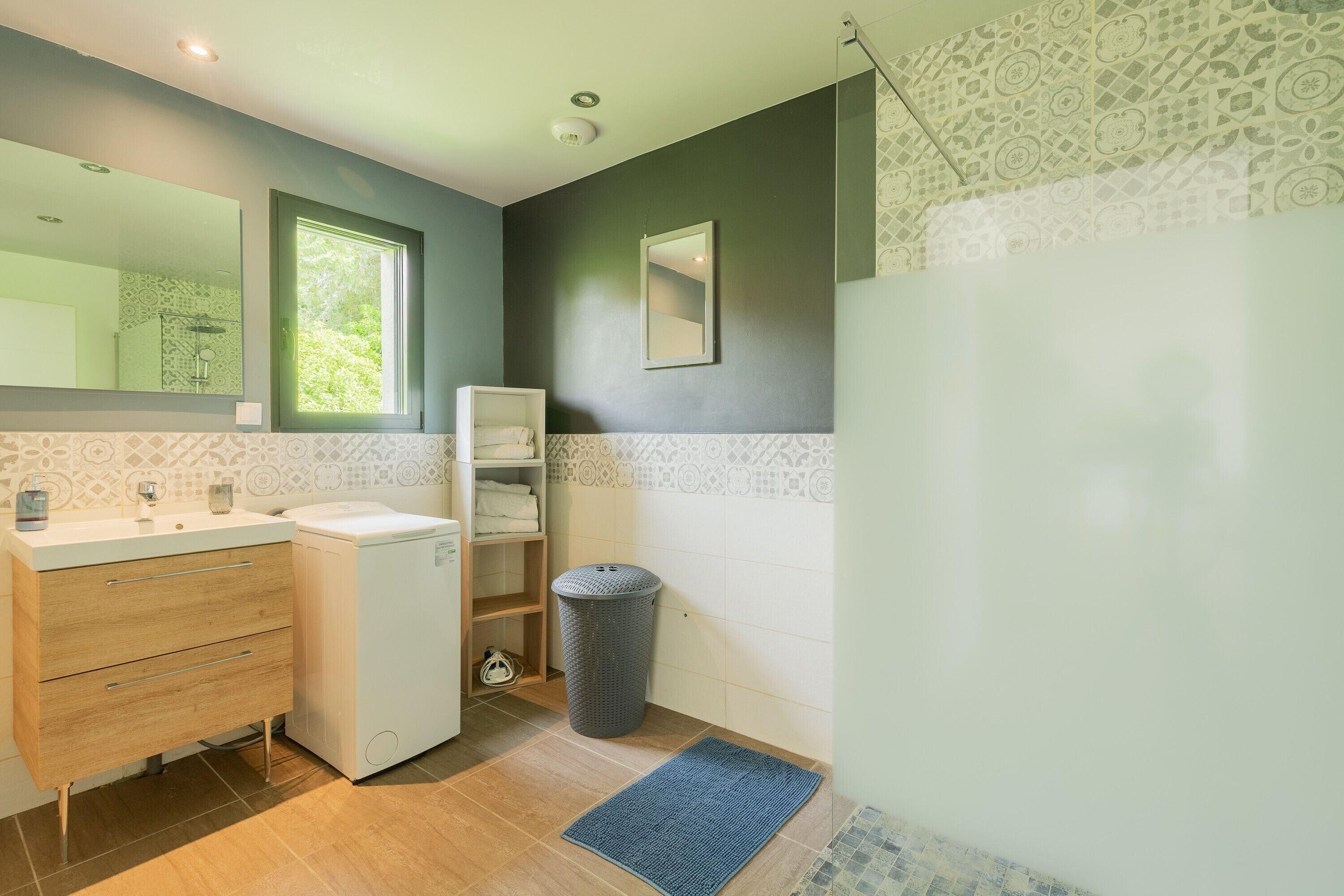 Een badkamer met een wastafel, spiegel, handdoekrek en een prullenbak.