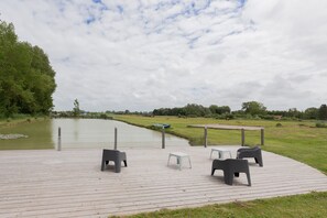 Una terraza de madera con mobiliario exterior, un pequeño bote y un cuerpo de agua tranquilo.