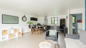 Ett modernt vardagsrum med en soffa, en matplats med stolar, ett kök med skåp och en tv som är monterad på väggen.
