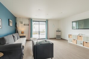 Una sala de estar moderna con sofá, una mesita, televisor y puerta corrediza de vidrio que da a un espacio al aire libre.