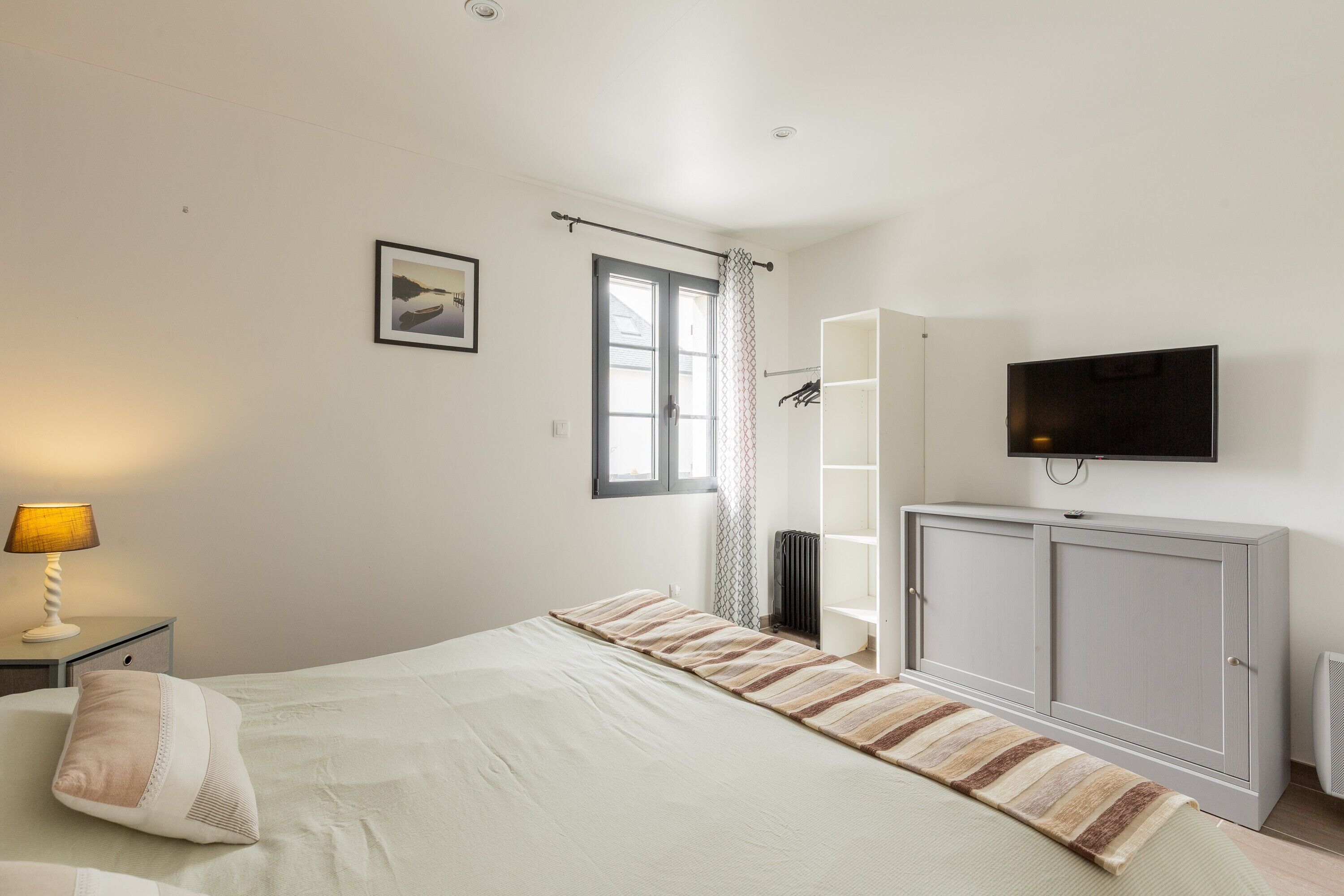 A bedroom with a bed, a TV mounted on the wall, a wardrobe, and a window with curtains.