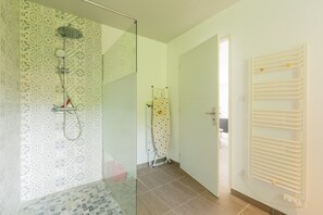 Un baño con baldosas estampadas, cabina de ducha con mampara de vidrio, toallero y una puerta que da a otra habitación.