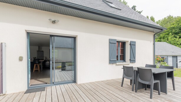 Ett modernt hus med en terrass, skjutdörrar i glas och utemöbler.