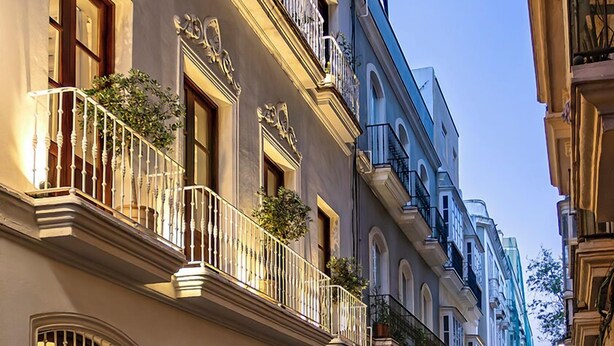 Une rue étroite bordée d’immeubles à plusieurs étages, dotés de balcons avec des garde-corps et de fenêtres avec des barreaux.