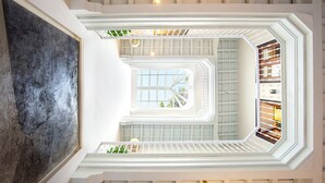 Un atrium à plusieurs niveaux, surmonté d’une verrière centrale, avec une grande peinture abstraite sur le côté gauche, et une vue sur l’intérieur à travers une paroi de verre.