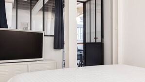 A modern hotel room with a large flat-screen TV, a bed with white bedding, a wardrobe, and a view of the balcony. - Bright & renovated: Haven of peace for 4 in Paris (Paris)