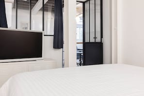 A modern hotel room with a large flat-screen TV, a bed with white bedding, a wardrobe, and a view of the balcony. - Bright & renovated: Haven of peace for 4 in Paris (Paris)