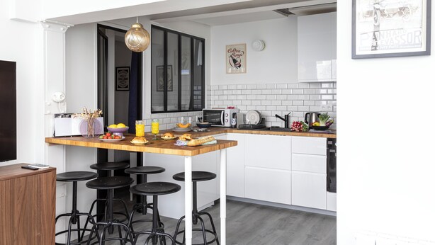 A modern kitchen with white cabinets, a wooden island with stools, a microwave, and a coffee machine. - Bright & renovated: Haven of peace for 4 in Paris (Paris)