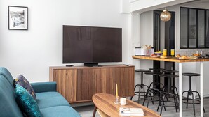 A modern living room with a sofa, a coffee table, a TV, and a dining area with stools. - Bright & renovated: Haven of peace for 4 in Paris (Paris)