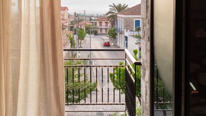 Un balcon donnant sur une rue, une voiture rouge et des bâtiments visibles au loin.