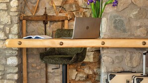 Un mur de pierres rustiques sur lequel est fixée une étagère en bois, et sur laquelle on peut voir un ordinateur portable, une chaise verte et un vase rempli de fleurs.