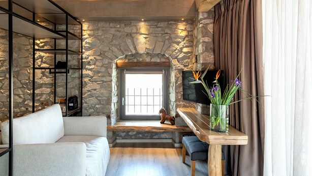 Une pièce chaleureuse avec un mur en pierre, un canapé, un téléviseur posé sur un meuble en bois et une fenêtre avec des rideaux.