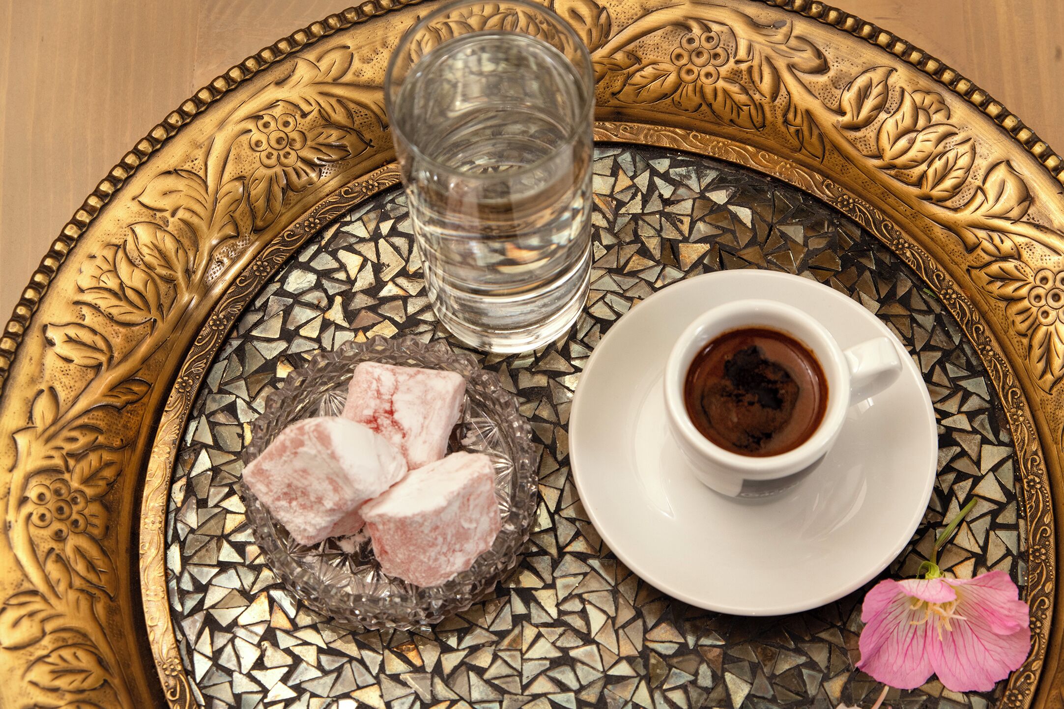 Una bandeja con un vaso de agua, una taza de café y un plato de lokum.
