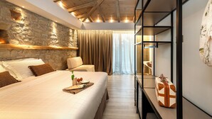 Une chambre avec un mur en pierre, un lit avec une literie blanche, un banc en bois et une valise posée sur une étagère.