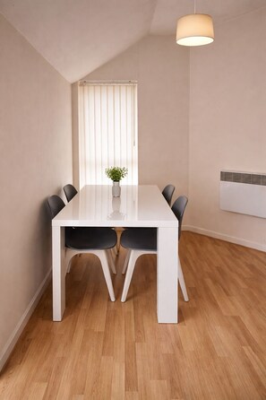 Un comedor con una mesa blanca, sillas negras, una planta en maceta y una lámpara en el techo.