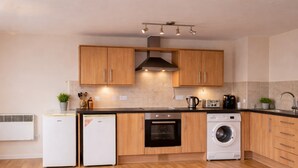 A modern kitchen with wooden cabinets, a built-in oven, a washing machine, and a compact refrigerator. - Webster Road Park Loft Apartment (Liverpool)