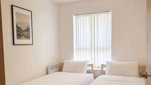 A room with two single beds, a ceiling lamp, a window with blinds, and a framed picture on the wall. - Webster Road Park Loft Apartment (Liverpool)
