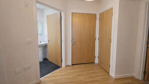 A hallway with wooden flooring, a door, and a bathroom visible through an open door. - Webster Road Park Loft Apartment (Liverpool)