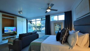 Ein Hotelzimmer mit Bett, Sofa, Fernseher, Deckenventilator und großen Fenstern.