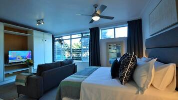 A hotel room with a bed, a sofa, a TV, a ceiling fan, and large windows.