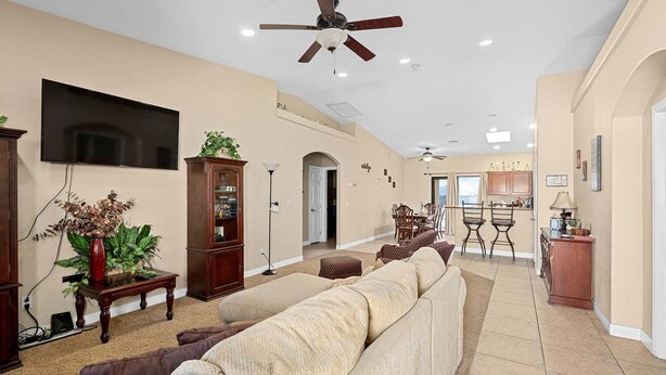 A spacious living room with a large sofa, a television, a ceiling fan, and a kitchen in the background. - Sabino Gorgeous Heatable Pool Retreat (Lake Havasu City)