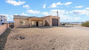 A single-story building with a garage, a gravel driveway, and a clear sky. - Sabino Gorgeous Heatable Pool Retreat (Lake Havasu City)