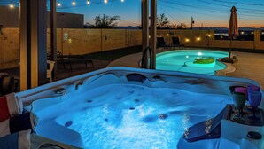 A hot tub with a view of a pool and mountains, surrounded by chairs and string lights. - Constellation of Havasu - Views, Pool, Spa (Lake Havasu City)
