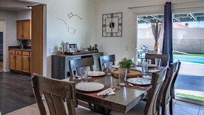 A dining area with a table set for four, wooden chairs, a clock on the wall, and a view of the outside. - Constellation of Havasu - Views, Pool, Spa (Lake Havasu City)