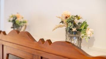 Un banco de madera con un respaldo decorativo, un espejo fijado a la pared y un jarrón con flores.