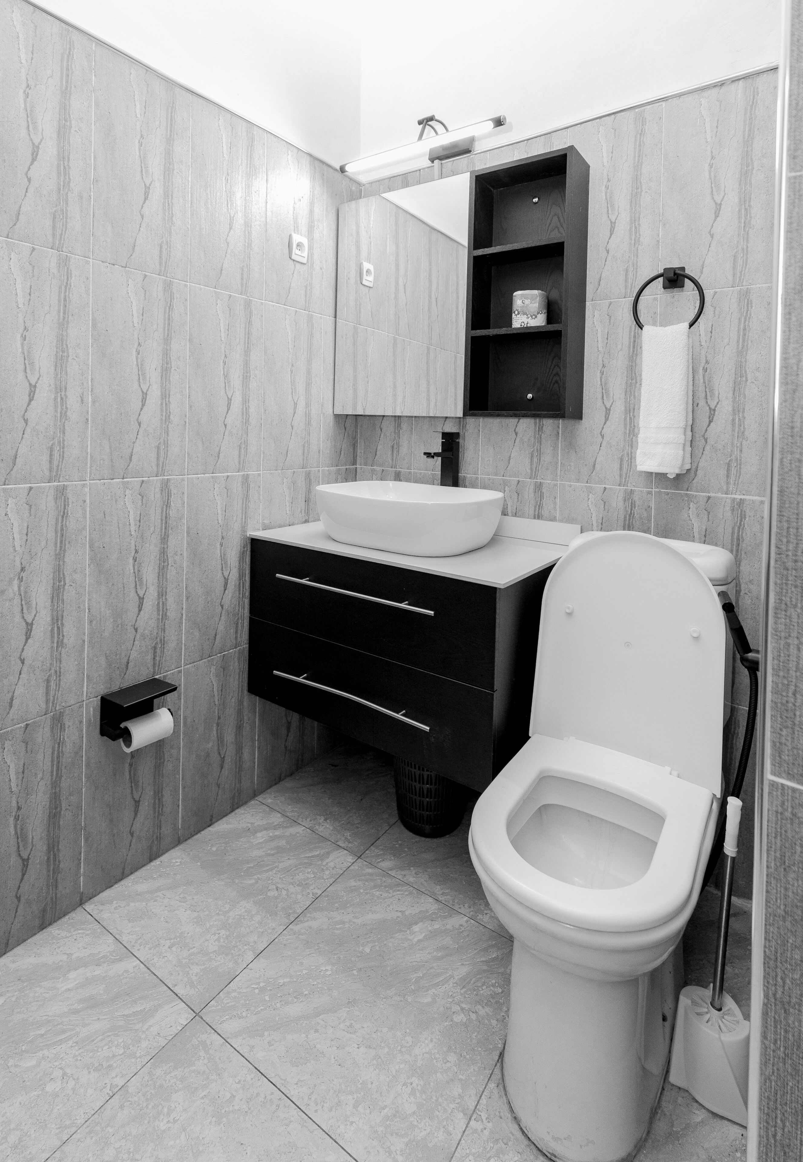 Une salle de bain moderne avec des toilettes blanches, un meuble-lavabo noir et un miroir au-dessus du meuble.