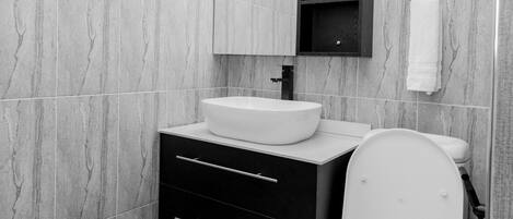 Une salle de bain moderne avec des toilettes blanches, un meuble-lavabo noir et un miroir au-dessus du meuble.