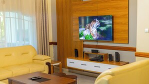 Moderni olohuone, jossa on keltainen sohva, puinen sohvapöytä, puiseen paneeliin kiinnitetty televisio ja pieni puinen sivupöytä.