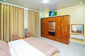 A hotel room with a bed, a wooden wardrobe, a television, a chair, and a mirror on the wall.
