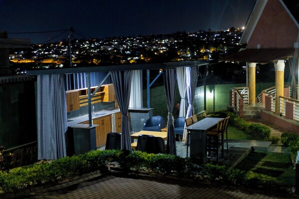 A patio area with a table and chairs, a small kitchen, and a view of a cityscape at night.