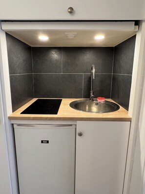 Eine kompakte Küche mit Spüle, einem schwarzen Induktionskochfeld und einem kleinen Schrank darunter.